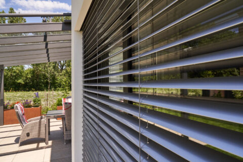 Moderne Aluminium Terrassenüberdachung mit passenden grauem Sonnenschutz (Aussenjalousien) an einem Einfamilienhaus in Lands…