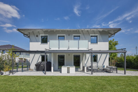 Modernes Einfamilienhaus mit offener Aluminium-Terrassenüberdachung und Lounge-Möbeln im Garten.