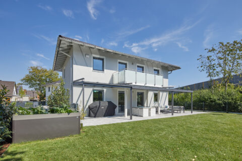 Modernes Einfamilienhaus mit anthrazitfarbener Terrassenüberdachung und Aufdachmarkisen, die eleganten Sonnenschutz bieten.