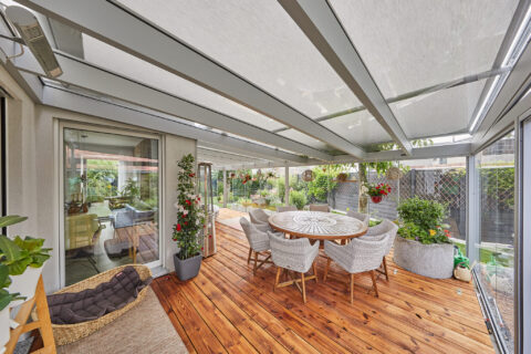 Moderner Aluminium-Kaltwintergarten mit Glasdach, integrierten Markisen und Holzterrasse in Zorneding, einladender Outdoor-W…