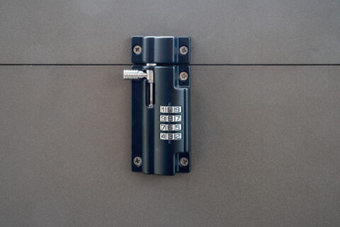 Nahaufnahme eines dunklen Zahlenschlosses mit silbernem Riegel, montiert auf einer grauen Fläche, symbolisiert Sicherheit un…