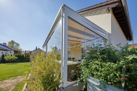 Moderner Kaltwintergarten aus Aluminium und Glas an einem Einfamilienhaus in Oberpframmern mit Beschattung und Gartenzugang.