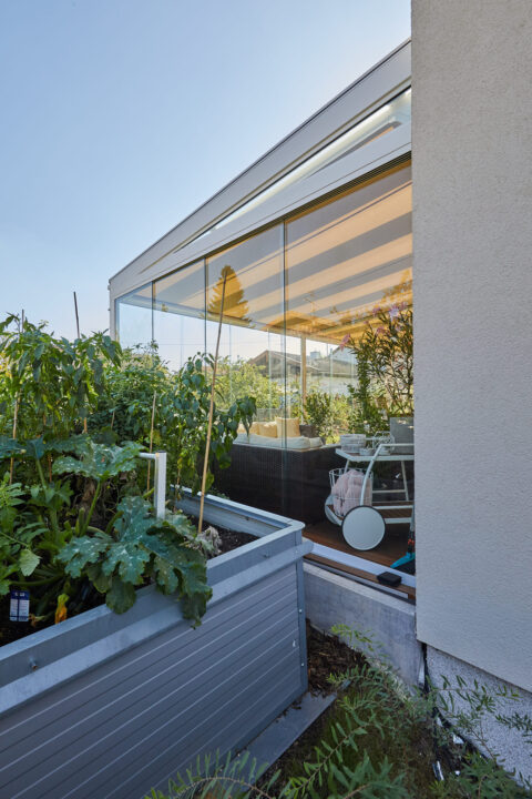 Kaltwintergarten auf Terrasse mit integrierter Markise und angrenzendem Hochbeet, schafft erweiterten Wohnraum und Gartenint…
