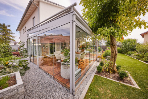 Moderner Kaltwintergarten mit vollständiger Glasfront und integrierter Beschattung, angrenzend an ein Einfamilienhaus in ein…