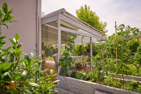 Moderner Kaltwintergarten mit gläsernen Schiebeelementen und grauem pulverbeschichtetem Rahmen an einem Wohnhaus in Zornedin…