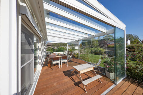 Moderner, barrierefreier Kaltwintergarten mit Glasschiebeelementen und Holzdielenterrasse, nahtloser Übergang zum Garten in…