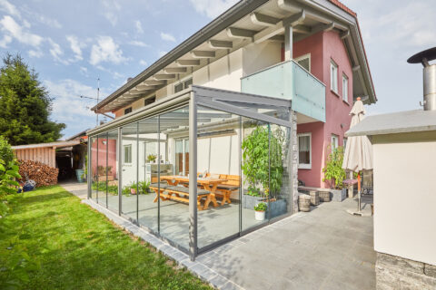 Moderner Kaltwintergarten mit flexiblen Glasschiebeelementen und integriertem Sonnenschutz an einem Wohnhaus in Kolbermoor.