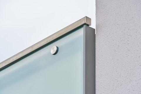 Detailansicht des Kantenschutzes an einem modernen Balkongeländer aus Sicherheitsglas, befestigt an einer Gebäudewand.