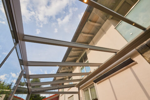 Moderne Terrassenüberdachung aus Aluminium und Glas an Hausfassade, mit integrierter Beleuchtung und Heizstrahler.