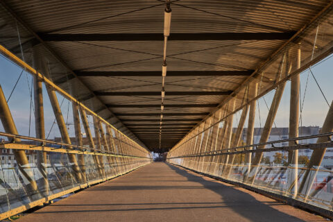 Überdachter Fußgängersteg am Bahnhof Mühldorf mit Glaswänden und Metallkonstruktion im warmen Abendlicht.
