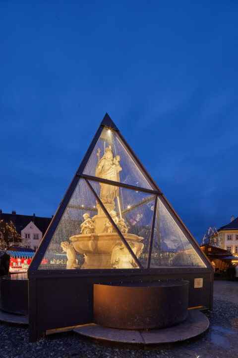 Marienbrunnen am Kapellplatz in Altötting, geschützt durch beleuchtete Glaspyramide.