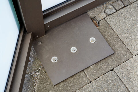 Detailansicht der robusten Aluminiumprofil-Befestigung einer maßgefertigten Terrasse auf gepflastertem Untergrund mit sichtb…