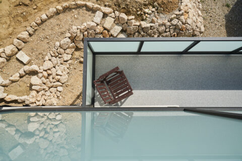 Vogelperspektive auf moderne Balkonüberdachung in Dorfen mit Aluminiumrahmen und Glas, daneben natürliche Steinlandschaft.