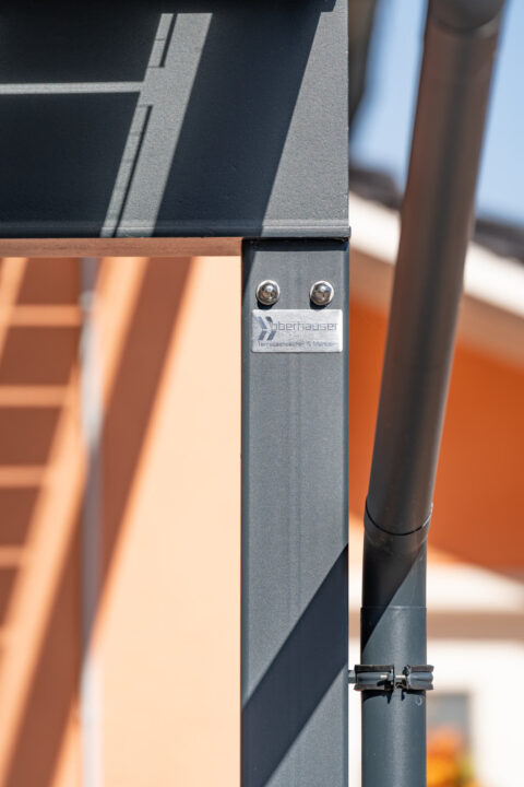 Detailansicht eines anthrazitfarbenen Metallpfostens eines Oberhauser PV-Carports mit Firmenlogo und Regenrinne.