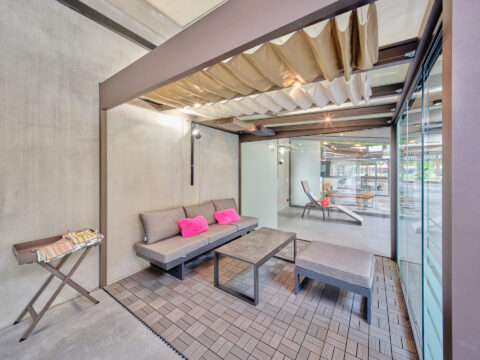 Moderner Wintergarten mit marronfarbener Seilspannmarkise, pulverbeschichtetem Aluminiumrahmen und Loungemöbeln.