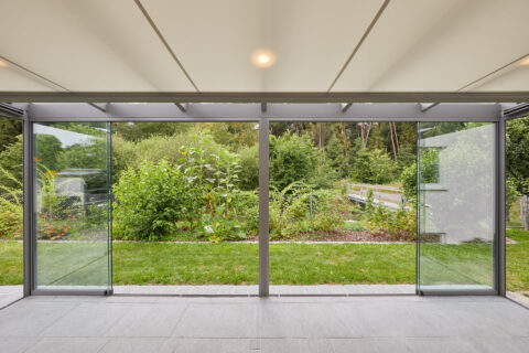 Geschlossene moderne Glas-Pergola mit eleganten Schiebeanlagen, die einen unverbauten Blick auf einen grünen Garten bietet.