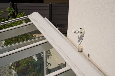Detailansicht eines Pfettenüberstands an einer Terrassenüberdachung aus Aluminium und Glas, mit Wettersensor.