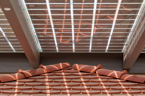 Photovoltaik-Dachelemente einer Terrassenüberdachung, die Sonnenlicht auf darunterliegende Ziegeldächer projizieren. Nachhal…