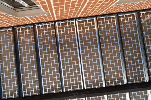 Detailansicht der Unterseite einer Photovoltaik-Überdachung mit sichtbaren Solarmodulen und strukturierten Lichtreflexionen.