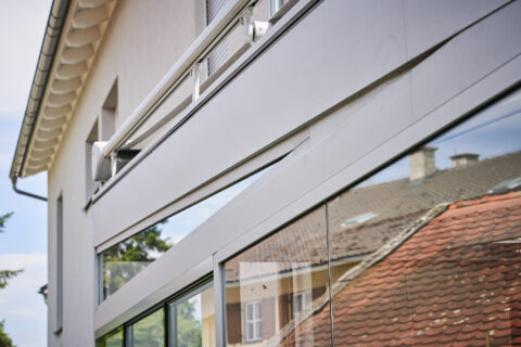 Moderne Terrassenüberdachung mit pulverbeschichtetem RAL-Rahmen und Ganzglas-Schiebeelementen an heller Hausfassade in Zorne…