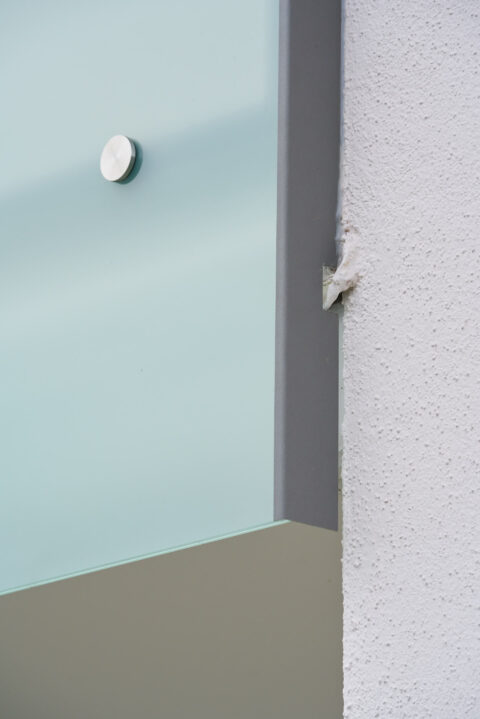 Edelstahl Punkthalter befestigt mattiertes Glaspaneel an einer Fassade, Detailansicht einer Balkonverglasung.