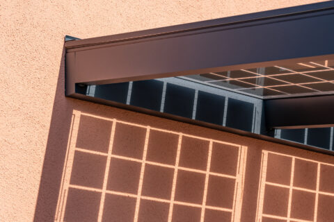 Detailaufnahme des Wandanschlusses eines modernen PV Carports mit Solarmodulen und Lichtschatten auf der Hauswand.
