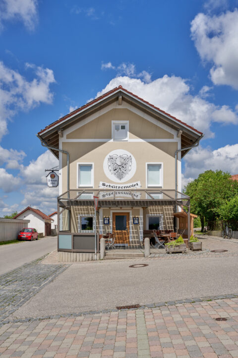 Gaststätte Schützenwirt Niederbergkirchen, Fassade mit Outdoor-Sitzbereich. Photovoltaikanlage auf dem Dach.