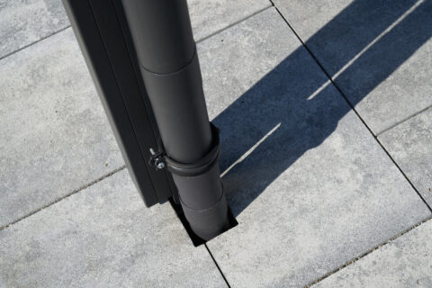 Dunkles Regenfallrohr einer Terrassenüberdachung elegant in gepflasterten Terrassenboden integriert.