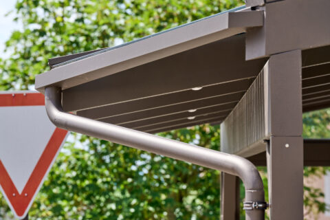 Nahaufnahme einer braunen Aluminium-Regenrinne und Fallrohrs an einem modernen Terrassendach aus Glas, für effizientes Wasse…