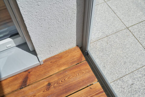 Nahaufnahme präziser Wandanschluss eines Seilicher Kaltwintergartens mit Schiebeelementen, Holzdielen und Terrassenplatten.