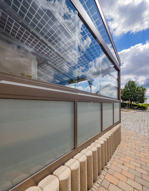 Moderne seitliche Glas- und Aluminiumverglasung einer Terrassenüberdachung mit integrierten PV-Modulen für Gastronomie.