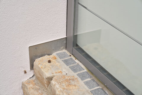 Detailansicht der seitlichen Verglasung einer Terrassenüberdachung mit Aluminiumprofil und Steinverblendung am Sockel.