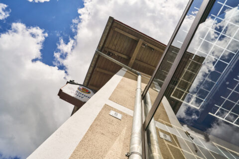 Seitliche Verglasung einer Terrasse mit Solarpanel-Integration, blaue Himmelsreflexionen und Gebäude des Schützenwirts.