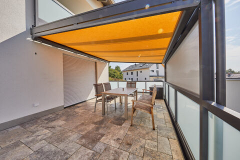 Balkon mit orangefarbener Pergola-Markise und seitlichem VertiTex Sonnenschutz von Weinor in Dorfen.