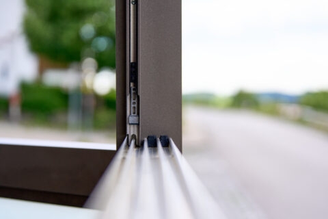 Detailansicht des Schiebesystems einer Glas-Terrassenüberdachung mit braunem Rahmen und Laufrollen für seitlichen Wetterschu…