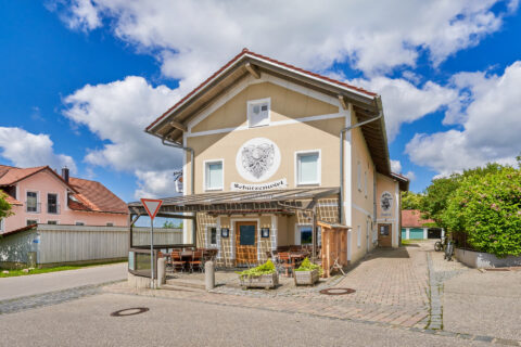 Traditionelle Gaststätte Schützenwirt in Niederbergkirchen mit modernem Glasdach-Außenbereich unter blauem Himmel.