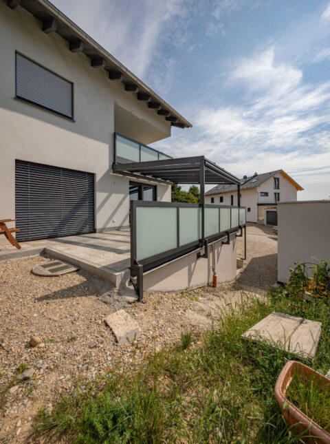 RAL pulverbeschichtete Aluminium-Terrassenüberdachung mit Milchglas-Brüstung an moderner Hausfassade in Dorfen.