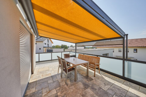 Moderne Balkonüberdachung mit orangefarbenem Sonnenschutz-Markisentuch und Glasgeländer in Dorfen