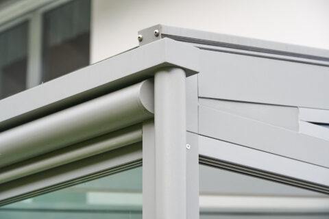 Detailansicht einer modernen Terrassenüberdachung aus hellgrauem Aluminiumprofil mit Glaselementen, sichere Konstruktion.