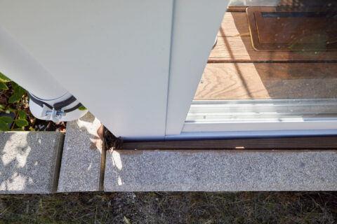 Detailansicht einer pulverbeschichteten Stütze einer Terrassenüberdachung mit Entwässerungsrohr auf Pflastersteinen.