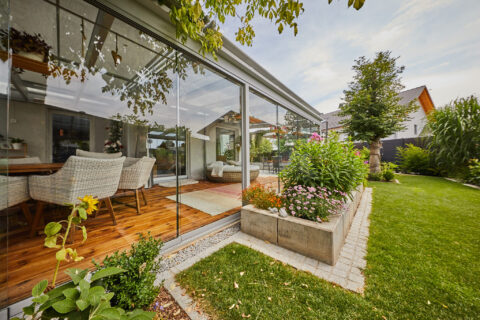Barrierefreie Glas-Schiebeanlage auf Holzterrasse, nahtloser Übergang zum Garten. Moderne Terrassenüberdachung in Zorneding.