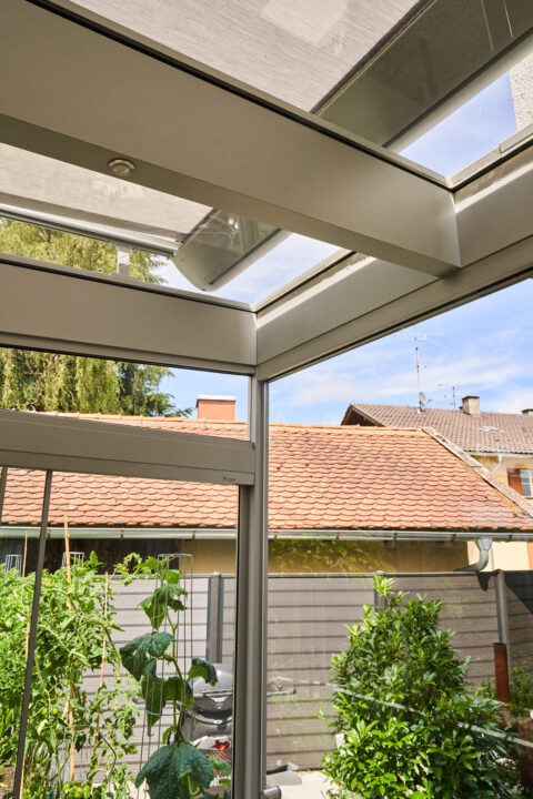 Detaillierte Ansicht eines Wintergartens mit Glasdach und seitlichen Verglasungen, Blick auf begrünten Gartenbereich und Däc…