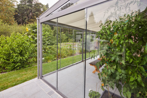 Moderner Kaltwintergarten aus Aluminium und Glas mit transparenten Schiebetüren für eine ganzjährigen Terrassenbereich.