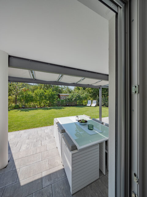 Moderne Terrassenüberdachung mit ausfahrbarem Sonnenschutz über einem eleganten Esstisch im grünen Garten.