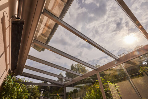 Modernes Terrassendach aus Aluminium mit Klarglas, integrierter Unterdachmarkise sowie Glasschiebeelemente.