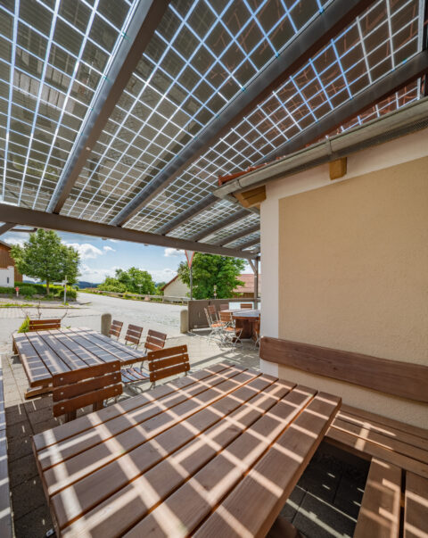 Ein Solarterrassendach über einem Biergarten mit Holztischen und -bänken, spendet Schatten und erzeugt Energie.
