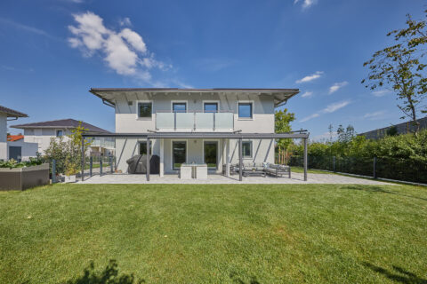 Modernes Einfamilienhaus in Feldkirchen mit eleganter Terrassenüberdachung und Balkon mit Glasgeländer.