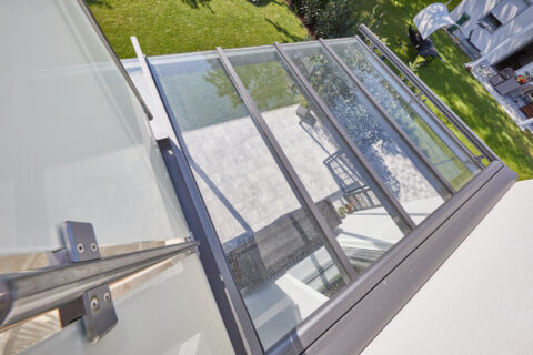 Detaillierte Ansicht einer modernen Glas-Terrassenüberdachung mit seitlichem Wandanschluss und Balkonintegration.