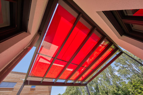 Moderne Terrassenüberdachung aus Aluminium mit integrierter roter Markise bietet optimalen Sonnenschutz.