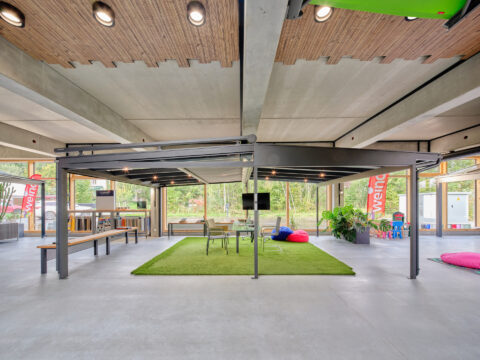 Terrassenüberdachung mit Satteldach, integrierter Aufdachmarkise und Senkrechtmarkise in moderner Ausstellungshalle.